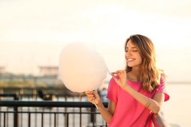 Happy young woman with cotton candy on waterfront