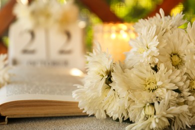 Photo of Beautiful white chrysanthemum flowers and open book on light grey table, closeup. Space for text