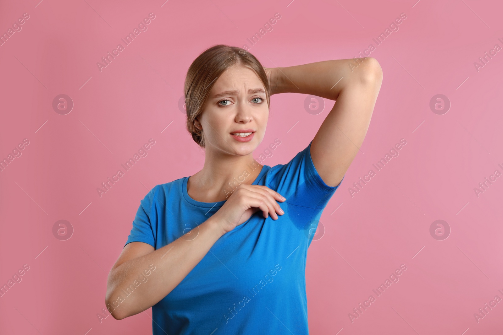 Photo of Young woman with sweat stain on her clothes against pink background. Using deodorant