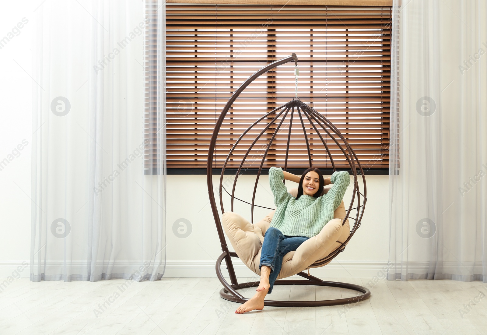 Photo of Young woman relaxing in hanging chair near window at home