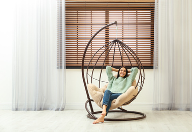 Photo of Young woman relaxing in hanging chair near window at home