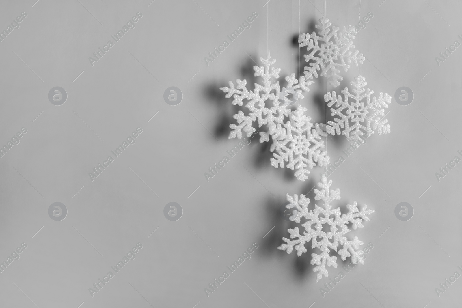 Photo of Beautiful decorative snowflakes hanging on light grey background, space for text