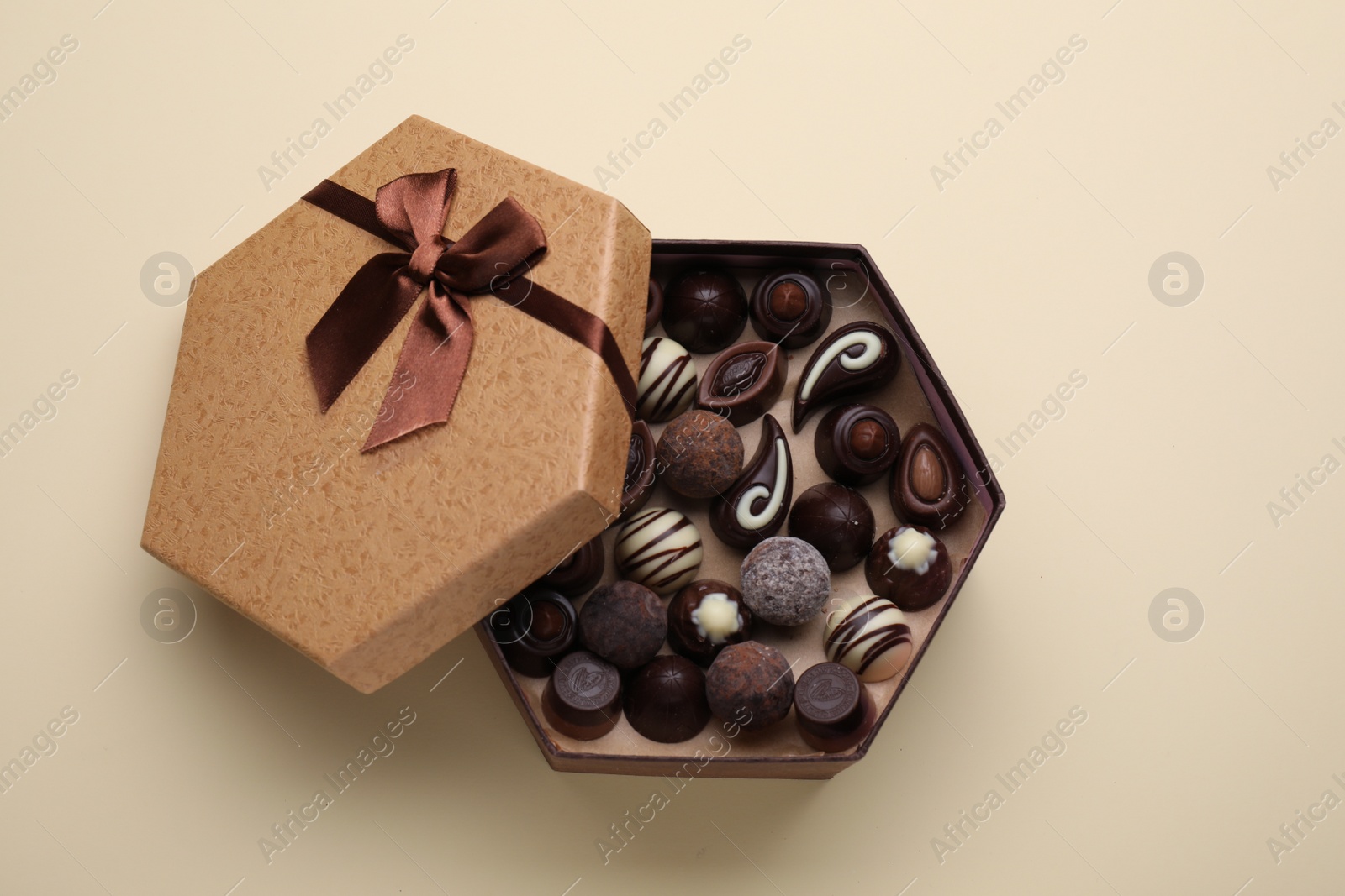 Photo of Open box of delicious chocolate candies on beige background, top view