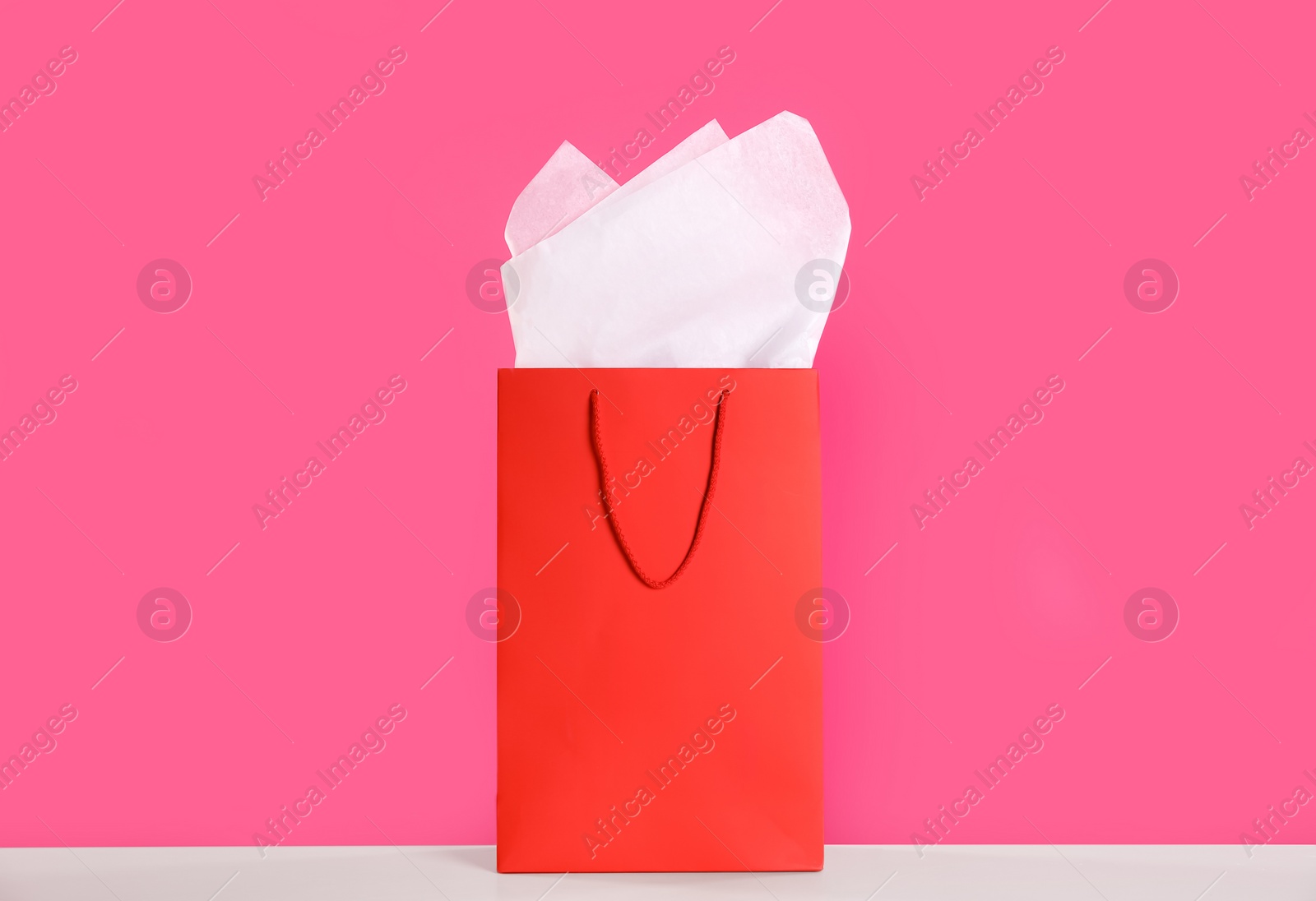 Photo of Gift bag with paper on white table against pink background