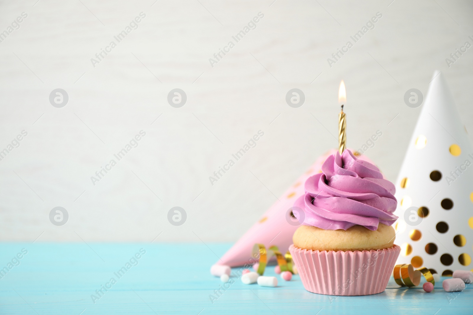 Photo of Delicious birthday cupcake with burning candle on light blue wooden table. Space for text