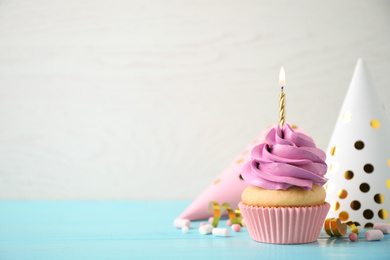 Photo of Delicious birthday cupcake with burning candle on light blue wooden table. Space for text