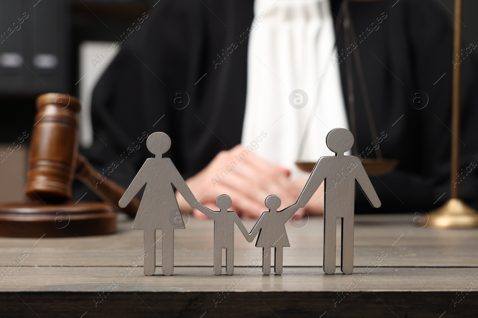 Photo of Family law. Judge with gavel sitting at wooden table, focus on figure of parents and children