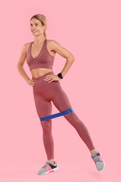 Woman exercising with elastic resistance band on pink background