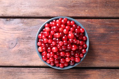 Photo of Fresh ripe cranberries in bowl on wooden table, top view