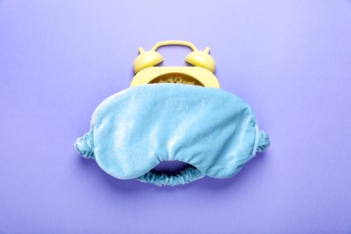 Soft sleep mask and alarm clock on purple background, top view