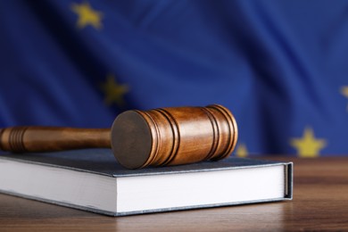 Photo of Judge's gavel and book on wooden table against European Union flag, closeup