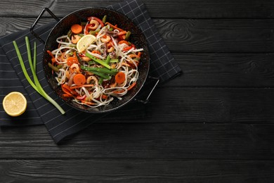 Photo of Shrimp stir fry with noodles and vegetables in wok on black wooden table, top view. Space for text