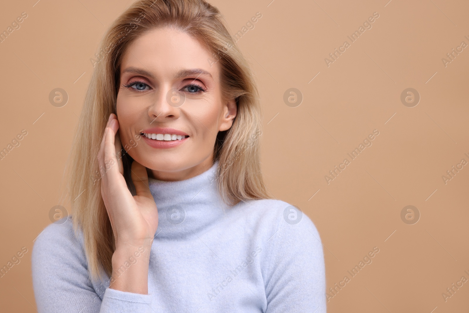 Photo of Portrait of smiling middle aged woman with blonde hair on beige background. Space for text