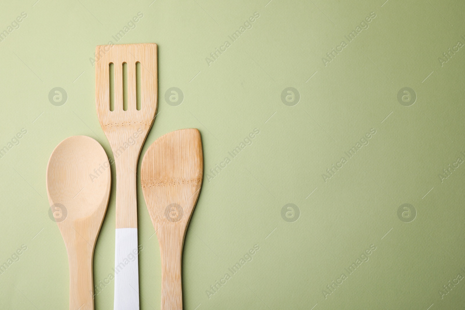 Photo of Wooden kitchen utensils on light olive background, flat lay. Space for text