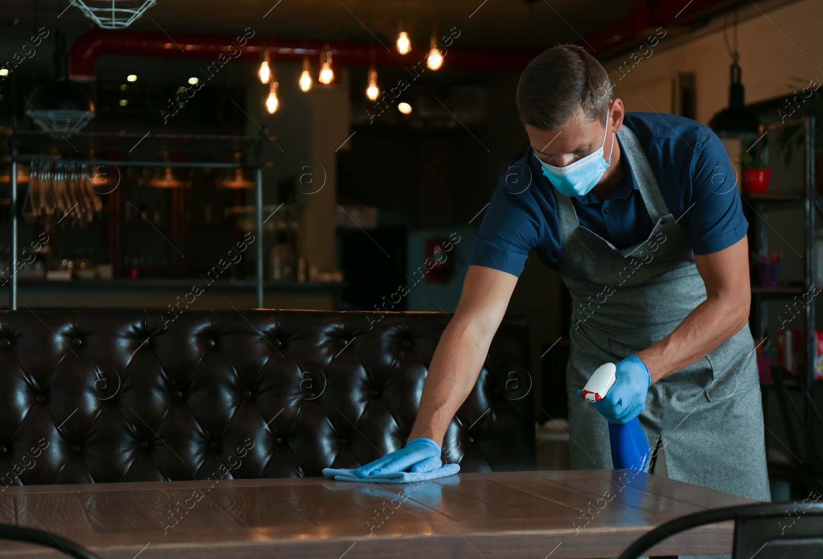 Photo of Waiter in mask and gloves disinfecting table at cafe