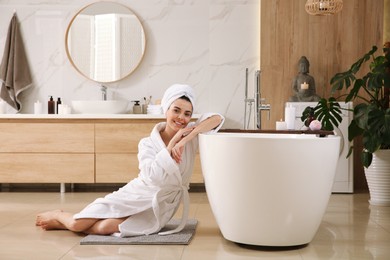 Beautiful young woman sitting near tub in bathroom