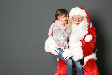 Photo of Little girl whispering in authentic Santa Claus' ear on grey background