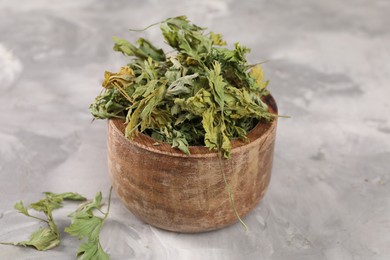 Photo of Bowl with dry parsley on light grey textured table, closeup