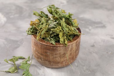 Bowl with dry parsley on light grey textured table, closeup