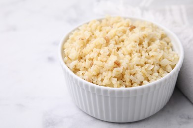 Photo of Cooked bulgur in bowl on white marble table, closeup. Space for text