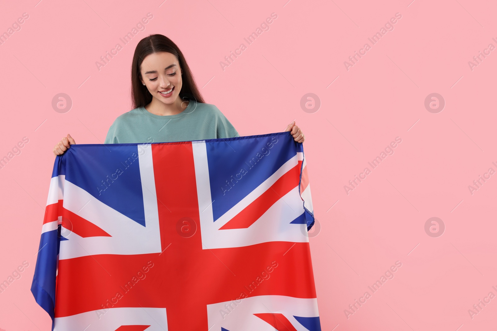 Photo of Young woman holding flag of United Kingdom on pink background, space for text