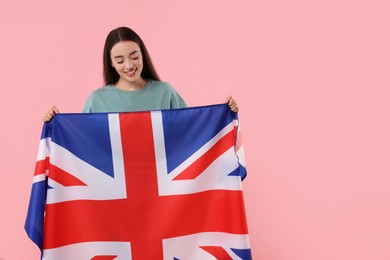 Photo of Young woman holding flag of United Kingdom on pink background, space for text