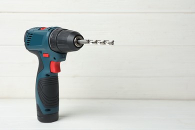 Photo of Modern electric power drill on white wooden table, space for text