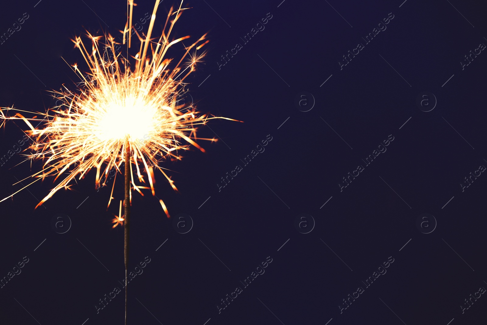 Photo of Bright burning sparkler on blue background, closeup. Space for text