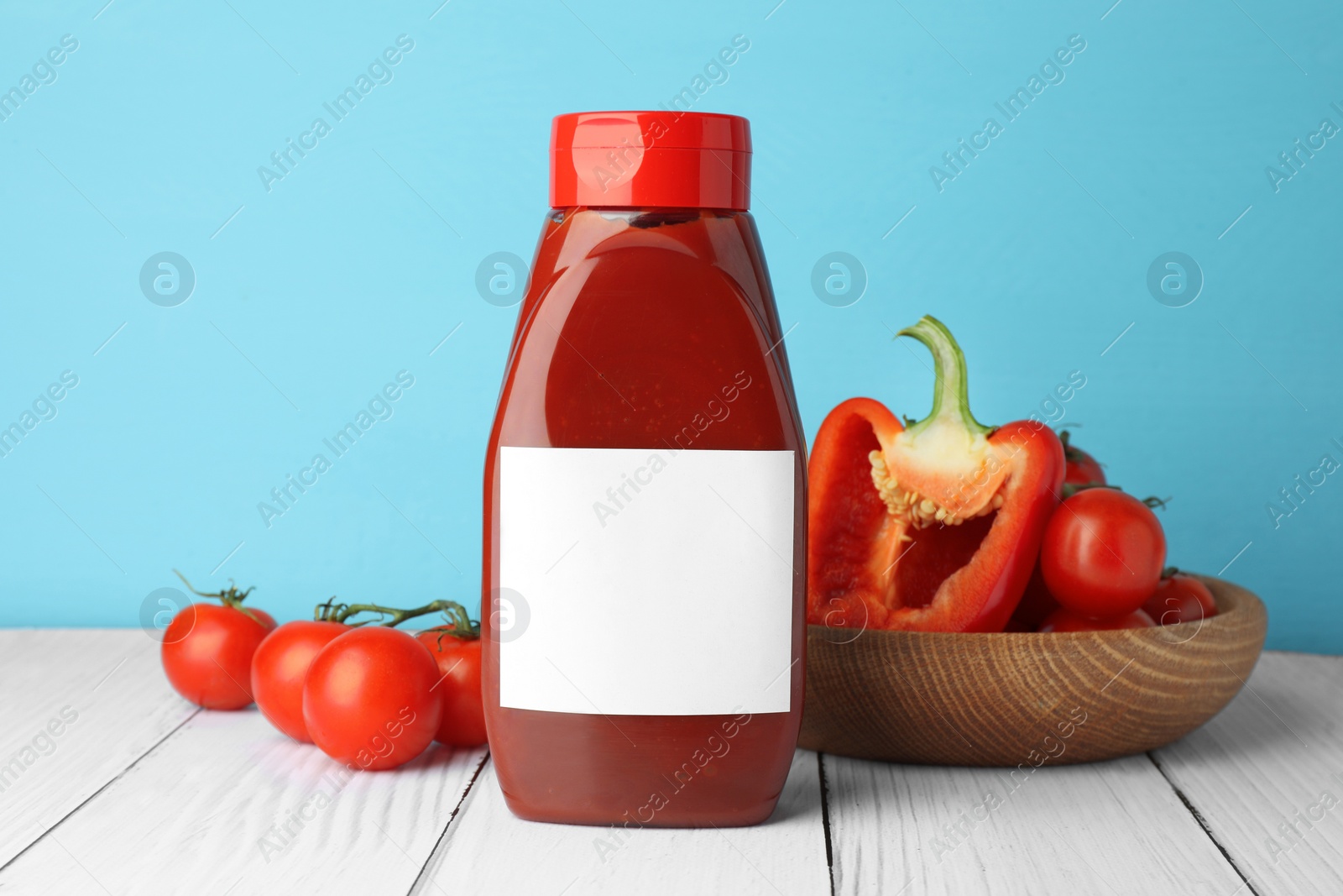 Photo of Bottle of tasty ketchup, tomatoes and pepper on white wooden table. Space for text