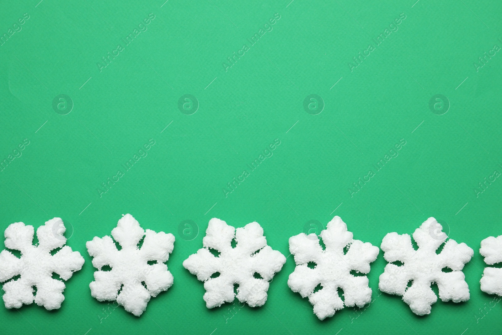 Photo of Beautiful decorative snowflakes on green background, flat lay. Space for text