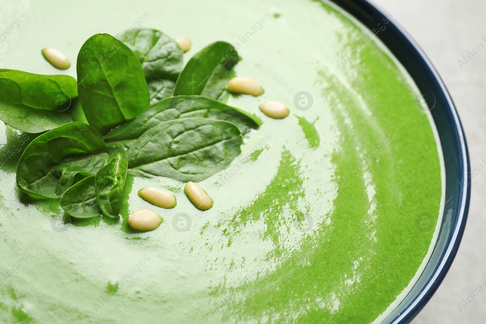 Photo of Bowl of healthy green soup with fresh spinach on grey table, closeup view