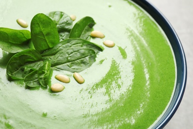 Bowl of healthy green soup with fresh spinach on grey table, closeup view