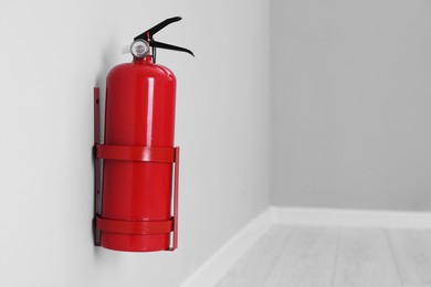 Photo of Fire extinguisher on light grey wall, space for text