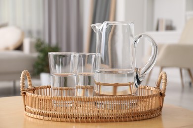 Jug and glasses with clear water on table indoors, closeup