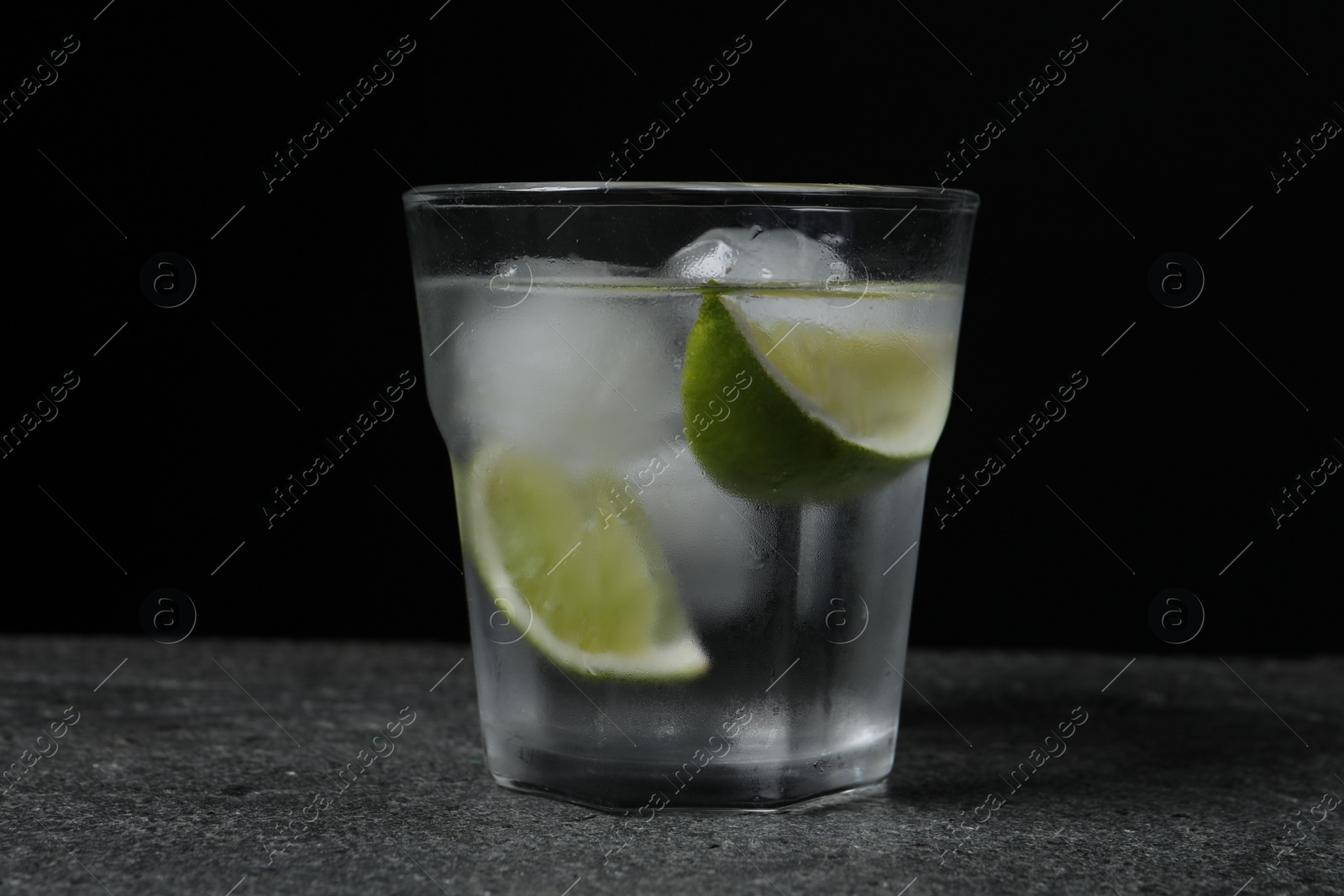 Photo of Glass of vodka with lime slices and ice on grey table