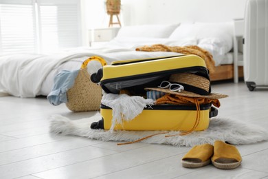 Photo of Open suitcase full of clothes, shoes and summer accessories on floor in room