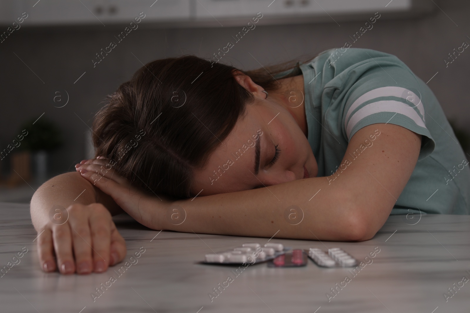 Photo of Woman sleeping at table with antidepressant pills and glass of water indoors