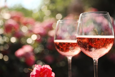 Photo of Glasses of rose champagne in blooming garden, closeup. Space for text