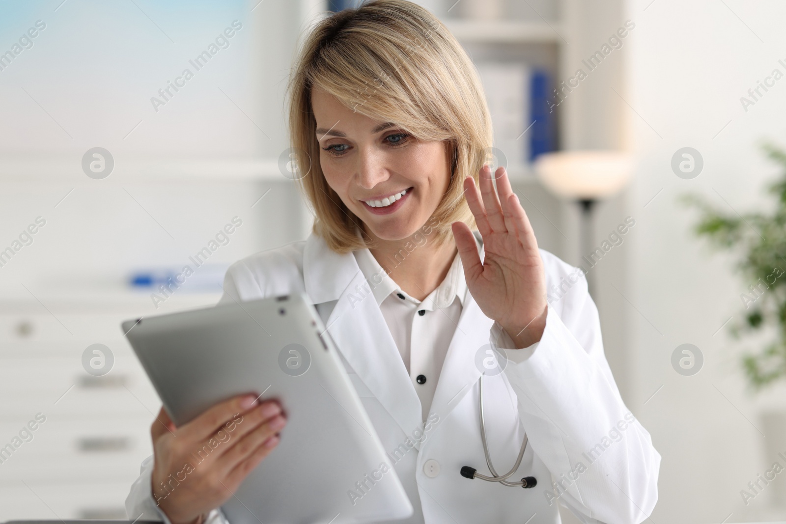 Photo of Smiling doctor with tablet having online consultation in office