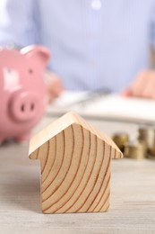 Photo of Woman planning budget at table, focus on wooden house model