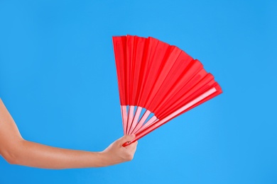 Photo of Woman holding red hand fan on light blue background, closeup