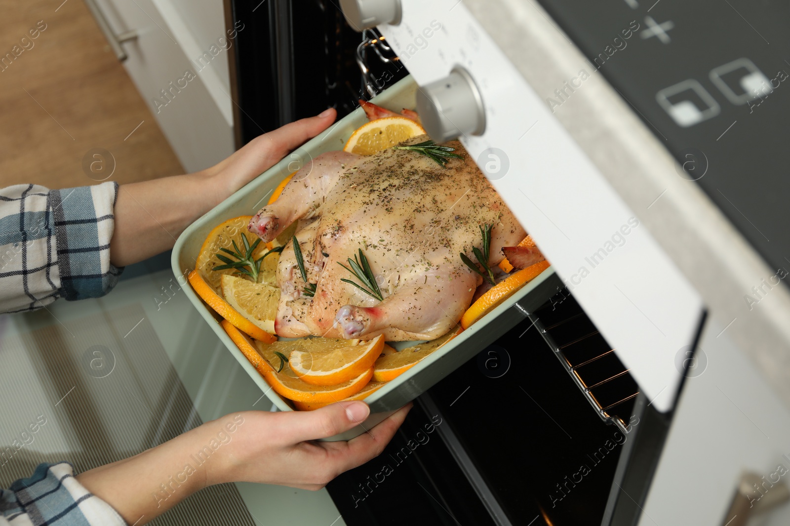 Photo of Woman putting chicken with orange slices into oven, closeup