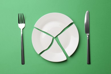 Photo of Pieces of broken ceramic plate and cutlery on green background, flat lay