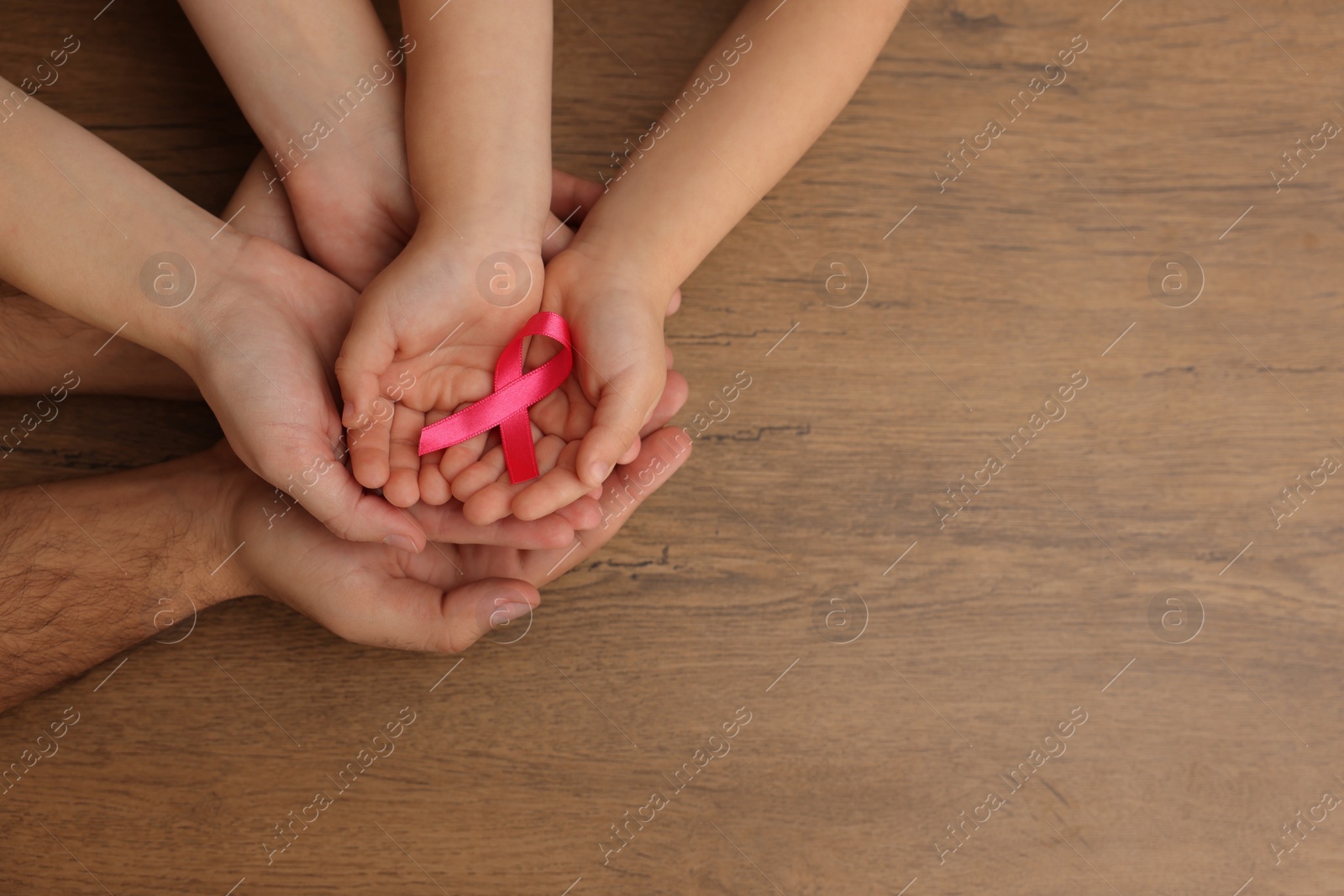 Photo of Family holding pink ribbon on wooden background, top view with space for text. Breast cancer awareness