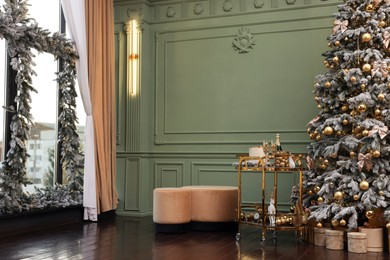 Beautiful Christmas tree, gift boxes, table and festive decor near olive wall indoors. Interior design
