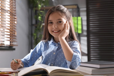 Photo of Pretty preteen girl doing homework at table