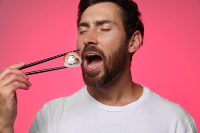 Photo of Handsome man eating tasty sushi roll with chopsticks on pink background