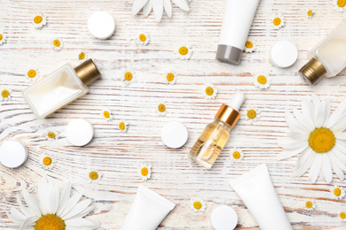 Flat lay composition with chamomile flowers and cosmetic products on white wooden table