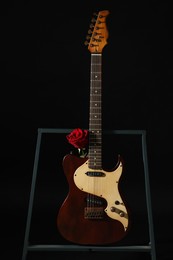 Beautiful rose near electric guitar on black background