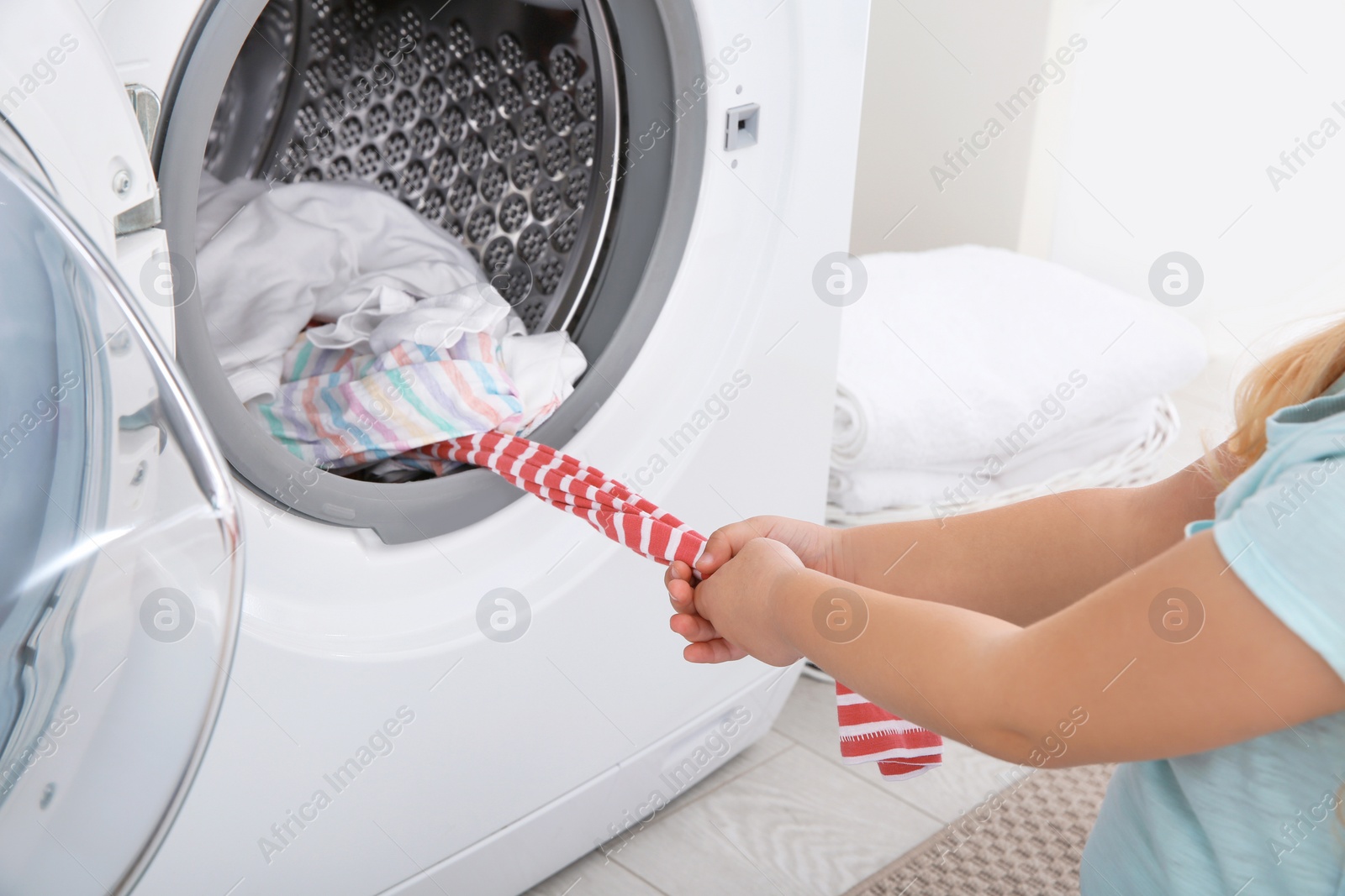 Photo of Adorable little girl taking clothes out of washing machine, closeup. Laundry day